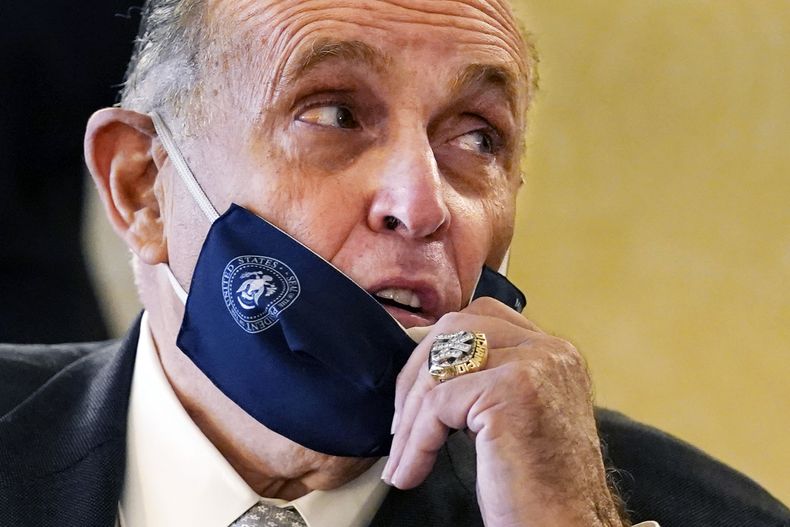 ARCHIVO — El exalcalde de Nueva York Rudy Giuliani, con un anillo de campeonato de los Yanquis de Nueva York, se baja la mascarilla para hablar con un asesor durante una conferencia de prensa en el Club de Mujeres Republicanos, el 16 de septiembre de 2020, en Nueva York. (AP Foto/Kathy Willens, Archivo)