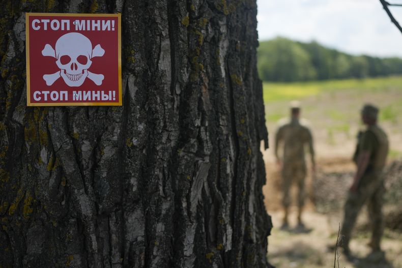 ARCHIVO - Un aviso sobre minas terrestres se ve en un árbol mientras un equipo ucraniano especializado busca minas en un campo a las afueras de Kiev, Ucrania, el jueves 9 de junio de 2022. (AP Foto/Natacha Pisarenko)
