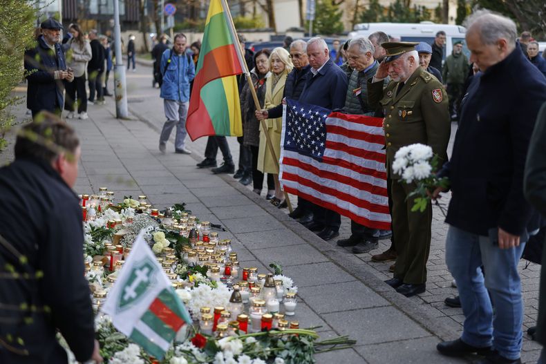 Personas con la bandera nacional estadounidense acuden a presentar sus condolencias a los tres soldados hallados muertos el lunes en un campo de entrenamiento de Pabrade, cerca de la embajada de Estados Unidos en Vilna, Lituania, martes 1 de abril de 2025. (AP foto/Mindaugas Kulbis)