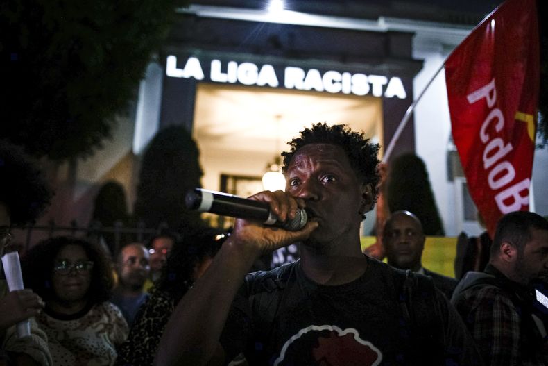 Delante de un mensaje proyectado en la fachada del consulado de España en Sao Paulo, un manifestante habla durante una protesta contra las expresiones racistas lanzadas a Vinícius Júnior, el martes 23 de mayo de 2023 (AP Foto/Tuane Fernandes)