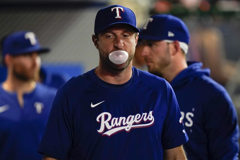 Max Scherzer, lanzador de los Rangers de Texas, hace una bomba con su goma de mascar en la caseta del equipo durante la segunda entrada del juego de béisbol en contra de los Angelinos de Los Ángeles, el lunes 25 de septiembre de 2023, en Anaheim, California. (AP Foto/Ryan S. Sun)