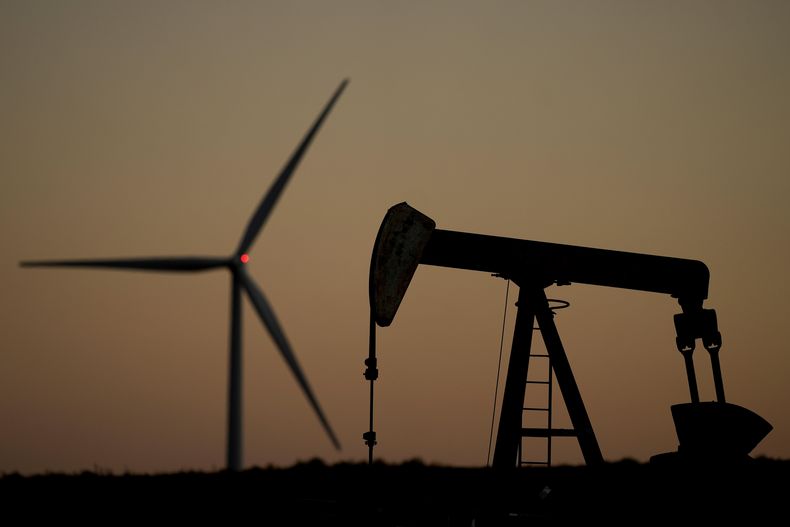 Una máquina de bombeo opera en primer plano mientras una turbina eólica en el parque eólico Buckeye Wind Energy se eleva en la distancia, el lunes 30 de septiembre de 2024, cerca de Hays, Kan. (Foto AP/Charlie Riedel)