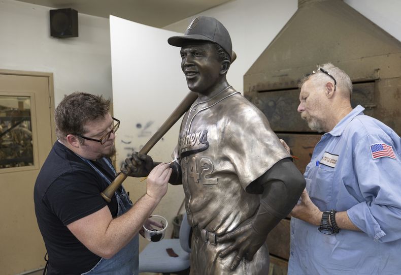 Nate Ford, a la izquierda, y Jeff Herndon dan los toques finales a una estatua del miembro del Salón de la Fama del béisbol y pionero de los derechos civiles Jackie Robinson en Loveland, Colorado, el miércoles 24 de julio de 2024. (Travis Heying/The Wichita Eagle vía AP)