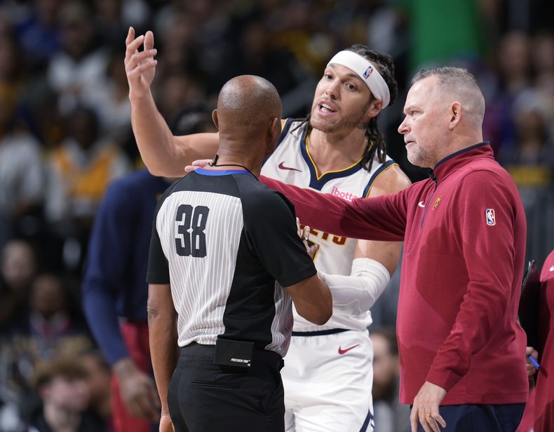 El alero Aaron Gordon, centro, de los Nuggets de Denver, discute con el árbitro Michael Smith, izquierda, después de que le marcara una falta, mientras el coach Michael Malone observa en la primera mitad del juego de baloncesto de la NBA en contra de los Warriors de Golden State, el lunes 25 de diciembre de 2023, en Denver. (AP Foto/David Zalubowski)