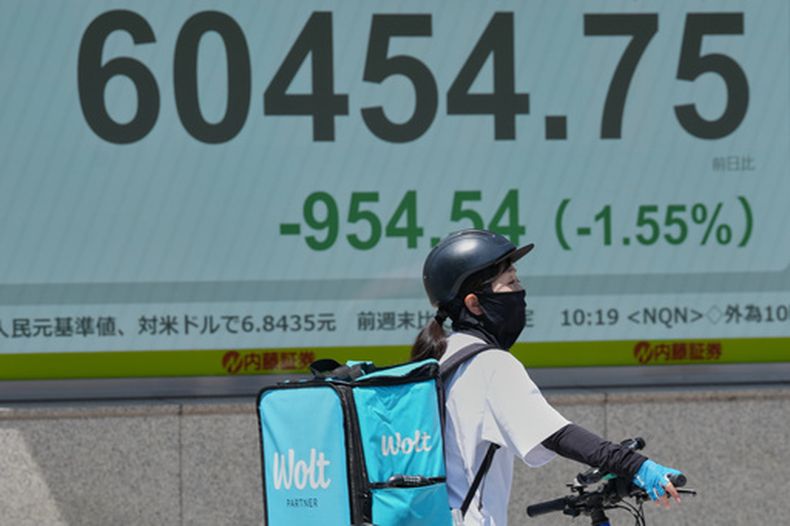 Una repartidora en bicicleta espera en un semáforo cerca de una pantalla electrónica que muestra el índice Nikkei de Japón en una firma de valores, el lunes 18 de mayo de 2026, en Tokio. (AP Foto/Eugene Hoshiko)