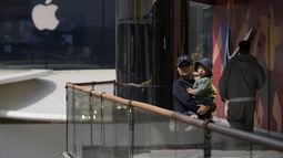 Una mujer sostiene a un niño en brazos cerca de las tiendas de Apple y Nike, el viernes 4 de abril de 2025, en Beijing, China. (AP Foto/Ng Han Guan)