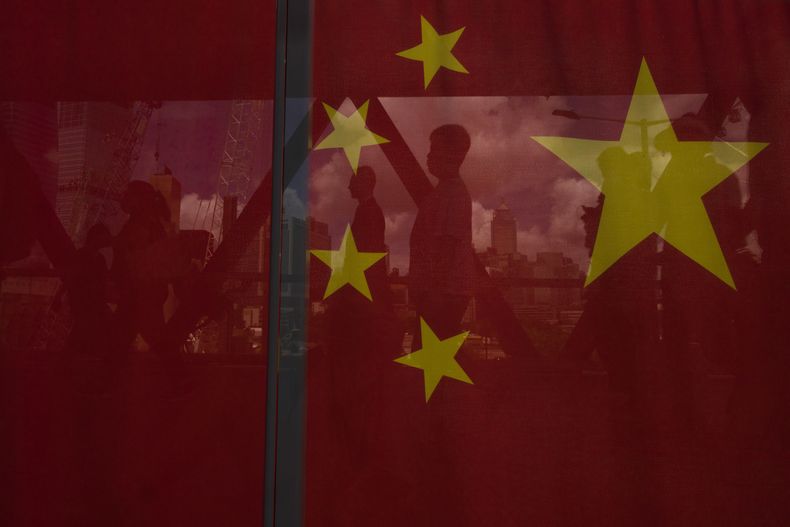 Peatones están reflejados en una bandera china en el 26 aniversario de la entrega de la ciudad por Gran Bretaña a China, Hong Kong, 27 de junio de 2023. (AP Foto/Louise Delmotte)