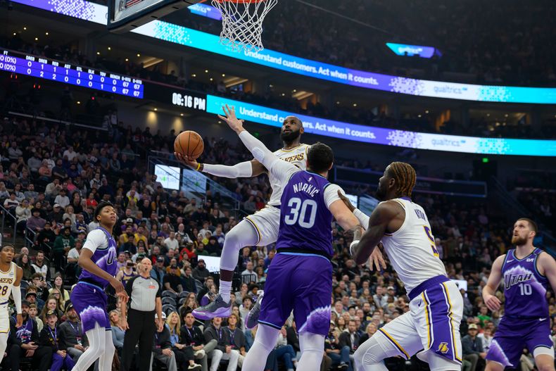 LeBron James, centro arriba, vuela rumbo a la canasta mientras Jusuf Nurkic (30), del Jazz de Utah, intenta defender durante la primera mitad del juego de baloncesto de la NBA, el domingo 23 de noviembre de 2025, en Salt Lake City. (AP Foto/Tyler Tate)