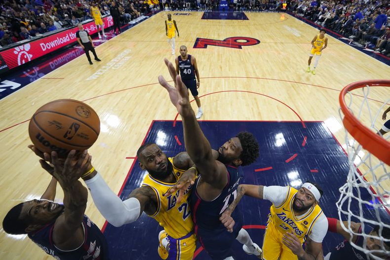 LeBron James, centro, de los Lakers de Los Ángeles, se alza para intentar un tiro entre DeAnthony Melton, izquierda, y Joel Embiid, de los 76ers de Filadelfia, durante la segunda mitad del juego de baloncesto de la NBA, el lunes 27 de noviembre de 2023, en Filadelfia. (AP Foto/Matt Slocum)