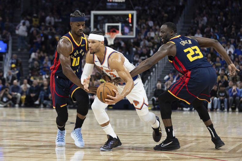 El alero de los Warriors de Golden State Jimmy Butler III (10) y el alero Draymond Green (23) defienden contra el escolta de los Knicks de Nueva York, Josh Hart, durante la primera mitad de un partido de baloncesto de la NBA, el sábado 15 de marzo de 2025, en San Francisco. (AP Foto/Benjamin Fanjoy)