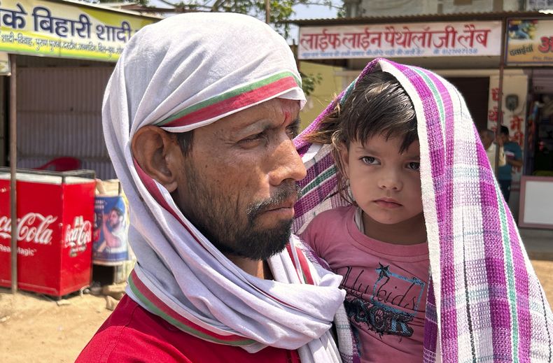 Un hombre camina con un niño en brazos, ambos cubiertos con pañuelos para protegerse de las altas temperaturas en plena ola de calor en Lalitpur, en el estado indio de Uttar Pradesh, el 17 de junio de 2023. (AP Foto/Rajesh Kumar Singh)