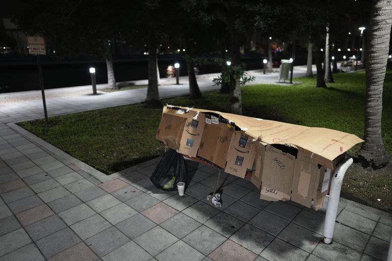 ARCHIVO - Una persona duerme dentro de un refugio improvisado en el banco de un parque en el centro de Miami, jueves 25 de enero de 2024. (AP Foto/Rebecca Blackwell, Archivo)