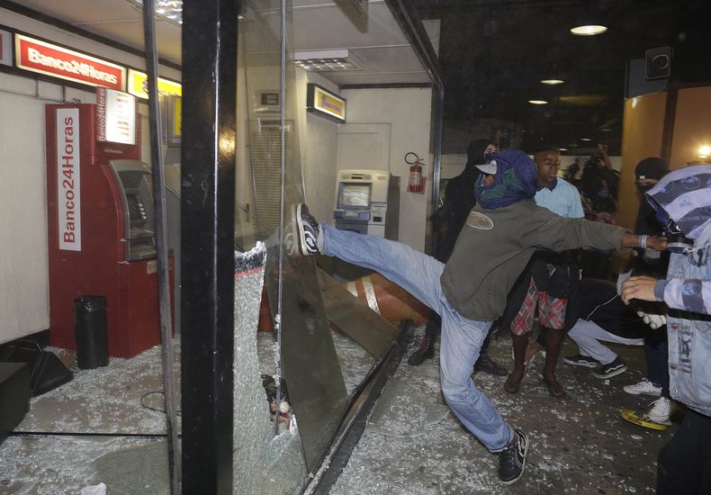 Anarquistas rompen ventanas cerca de cajeros autom&aacute;ticos dentro de una terminal de autobuses durante una protesta en Sao Paulo, Brasil, el viernes 25 de octubre de 2013. Los inconformes exigen transporte gratuito. (AP Foto/Andre Penner)