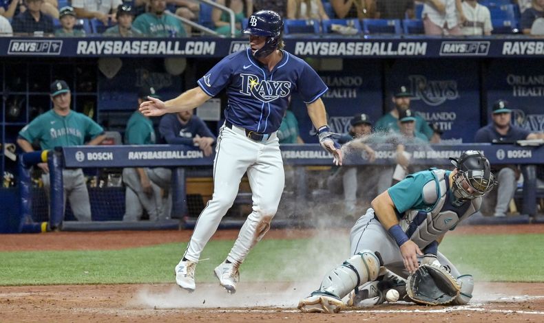 El jardnero Jonny DeLuca, de pie, de los Rays de Tampa Bay anota la carrera de la ventaja mientras el receptor de los Marineros de Seattle, Cal Raleigh, no puede controlar el tiro al plato durante la octava entrada del juego de béisbol del lunes 24 de junio de 2024, en San Petersburgo, Florida. (AP Foto/Steve Nesius)