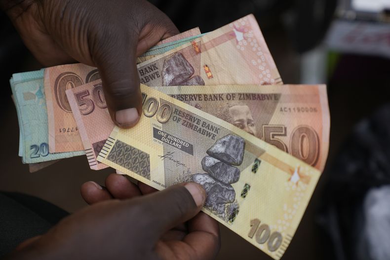 ARCHIVO - Un corredor de moneda sostiene billetes de diversas denominaciones de dólar zimbabuense en las calles de Harare, Zimbabue, el 9 de junio de 2022. (AP Foto/Tsvangirayi Mukwazhi, Archivo)