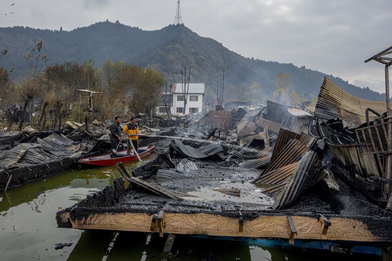 Civiles lanzan agua a los restos de casas flotantes de madera que fueron consumidas por un incendio estando ancladas en el lago Dal, en las afueras de Srinagar, en la Cachemira controlada por India, el sábado 11 de noviembre de 2023. (AP Foto/Dar Yasin)
