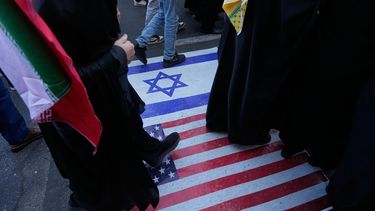 Manifestantes caminan sobre una representación de las banderas de EEUU e Israel durante una manifestación en Teherán, el martes 4 de noviembre de 2025. (AP Foto/Vahid Salemi)