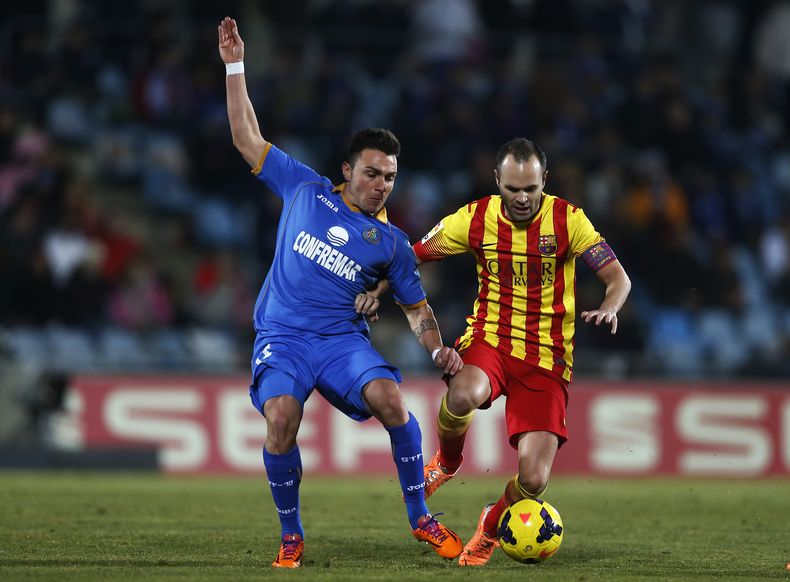 Andr&eacute;s Iniesta (der) supera la marca de Adri&aacute;n Colunga, de Getafe, en un partido de la liga espa&ntilde;ola el 22 de diciembre del 2013 en Madrid. Iniesta prorrog&oacute; su contrato con el Barcelona por otros tres a&ntilde;os, hasta el 2018