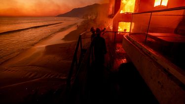 ARCHIVO - Bomberos trabajan desde una terraza mientras el incendio Palisades quema una propiedad frente a la playa el miércoles 8 de enero de 2025 en Malibú, California. (Foto AP/Etienne Laurent, archivo)