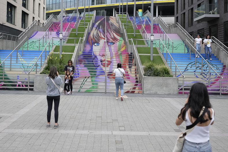 Fans posan junto a un retrato de Taylor Swift pintado en una escalera en el estadio de Wembley en Londres, el miércoles 14 de agosto de 2024, antes de una serie de conciertos de Taylor Swift que comienzan el jueves. (Foto AP/Alastair Grant)