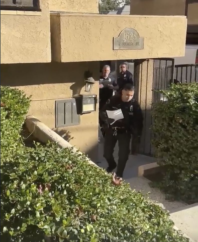 En este fotograma tomado de un video proporcionado por el abogado Dermot Givens, agentes del Departamento de Policía de Los Ángeles se acercan a Givens con una copia de una orden de registro fuera de su casa, en Los Ángeles, el martes 23 de enero de 2024. (Dermot Givens via AP)