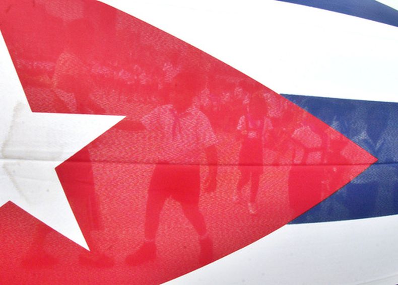 ARCHIVO - Niños caminan a través de la bandera cubana hacia el Malecón habanero para lanzar flores al mar en conmemoración del aniversario de la muerte del Comandante revolucionario cubano Camilo Cienfuegos, el jueves 28 de octubre de 2004 en La Habana, Cuba. (Foto AP/Cristóbal Herrera, Archivo)
