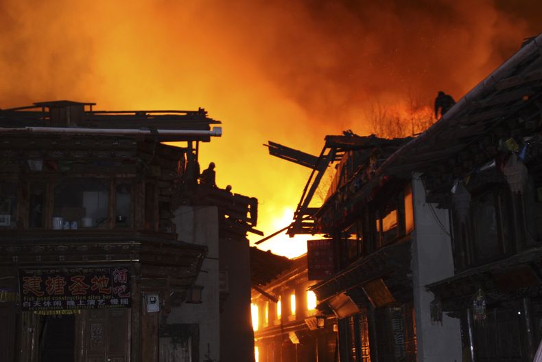 Bomberos combaten el incendio desde los techos de los edificios mientras las llamas destruyen el milenario poblado tibetano de Dukezong en el condado Shangri-La, en el suroeste de China, el s&aacute;bado 11 de enero de 2014. (Foto AP)