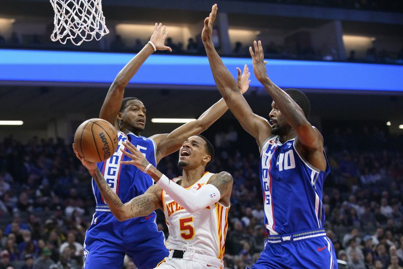 Dejounte Murray (5), de los Hawks de Atlanta, es marcado por DeAaron Fox, izquierda, y Harrison Barnes (40), de los Kings de Sacramento, durante la primera mitad del juego de baloncesto de la NBA en Sacramento, California, el lunes 22 de enero de 2024. (AP Foto/Randall Benton)