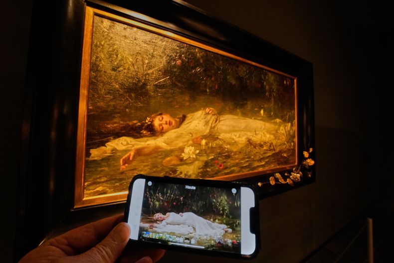 En el celular, el video de la canción The Fate of Ophelia de Taylor Swift, y al fondo, el cuadro en que se inspiró, obra de Friedrich Heyser, en un museo en Wiesbaden, Alemania, el 16 de octubre del 2025. (AP foto/Michael Probst)