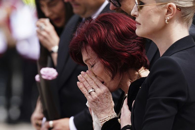 Sharon Osbourne recibe el apoyo de sus hijos Jack Osbourne y Kelly Osbourne mientras depositan y ven las flores colocadas en el banco del puente Black Sabbath en Broad Street en memoria del líder de Black Sabbath, Ozzy Osbourne, antes de su procesión fúnebre, en Birmingham, Inglaterra, el miércoles 30 de julio de 2025. (Jacob King/PA via AP)