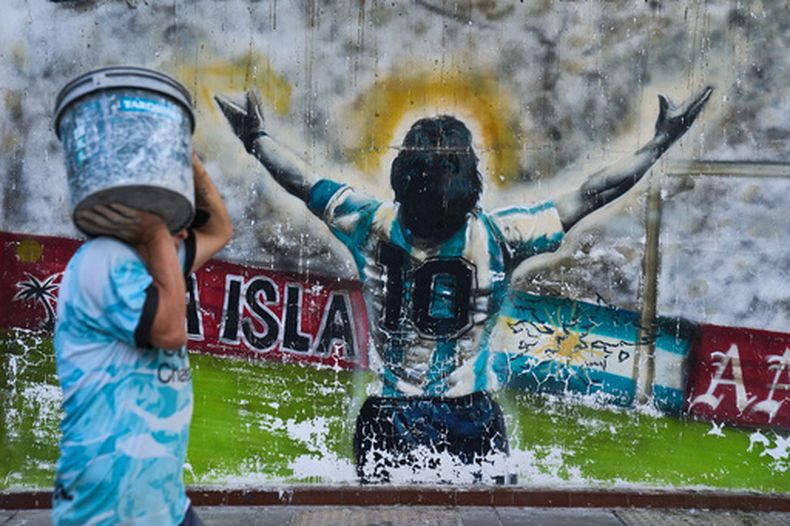 Un peatón pasa con un cubo junto a un grafiti que representa al fallecido futbolista Diego Maradona en Buenos Aires, Argentina, el lunes 13 de abril de 2026. (Foto AP/Rodrigo Abd)