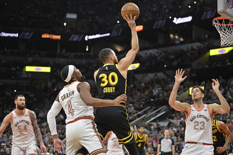 Stephen Curry (30), de los Warriors de Golden State, dispara ante las miradas de Devonte Graham (4) y Zach Collins (23), de los Spurs de San Antonio, durante la segunda mitad del juego de baloncesto de la NBA, el domingo 31 de marzo de 2024, en San Antonio. (AP Foto/Darren Abate)