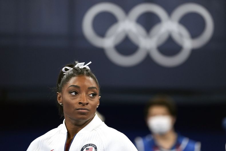 ARCHIVO - El 27 de julio de 2021, Simone Biles, de Estados Unidos, observa a las gimnastas actuar después de salir de la final por equipos en los Juegos Olímpicos de Verano de 2020, en Tokio. Biles, quien redefinió la excelencia en la gimnasia y obtuvo siete medallas olímpicas en el camino, llamó la atención y, de algunos, las críticas al retirarse de los eventos en Tokio debido a un bloqueo mental que le daba miedo intentar ciertos movimientos peligrosos. (AP Foto/Ashley Landis, Archivo)