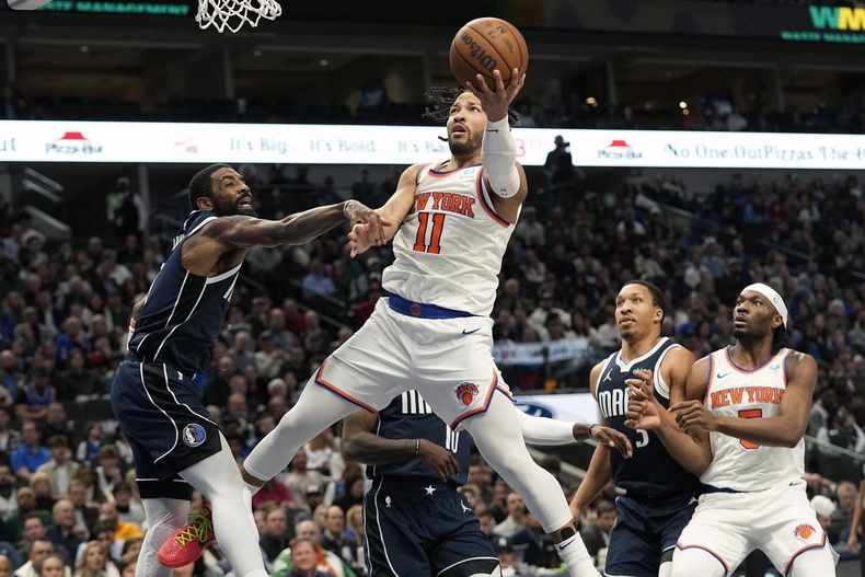 El escolta de los Knicks de Nueva York, Jalen Brunson, centro, encesta contra el escolta de los Mavericks de Dallas, Kyrie Irving, izquierda, durante la segunda mitad del partido de baloncesto de la NBA en Dallas, el jueves 11 de enero de 2024. (AP Foto/LM Otero)