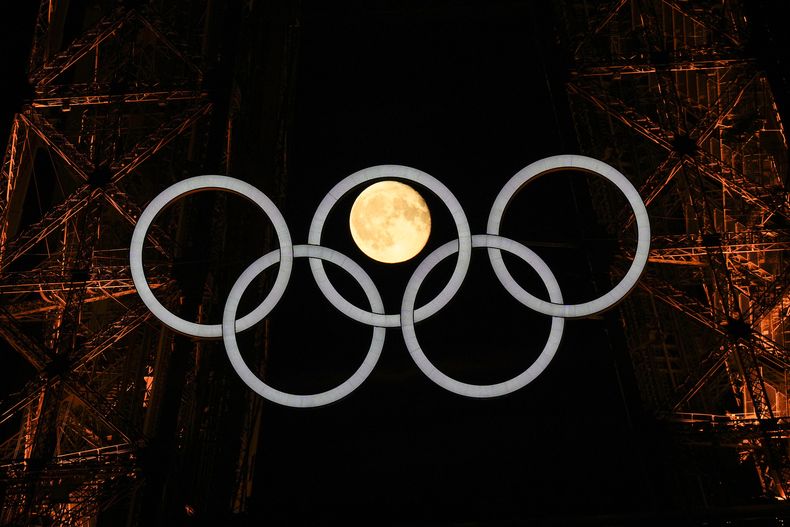 La Luna llena se aprecia detrás de los aros olímpicos en la Torre Eiffel el lunes 22 de julio de 2024 (AP Foto/David J. Phillip)