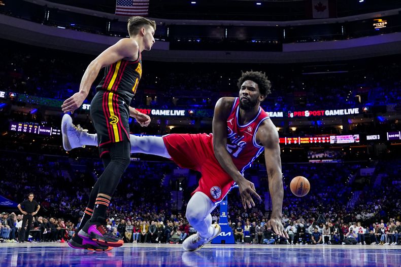 Joel Embiid de los 76ers de Filadelfia (derecha) pierde control del balón mientras cae próximo a Bogdan Bogdanovic de los Hawks de Atlanta durante la primera mitad del juego de la NBA, el viernes 8 de diciembre de 2023, en Filadelfia. (AP Foto/Chris Szagola)
