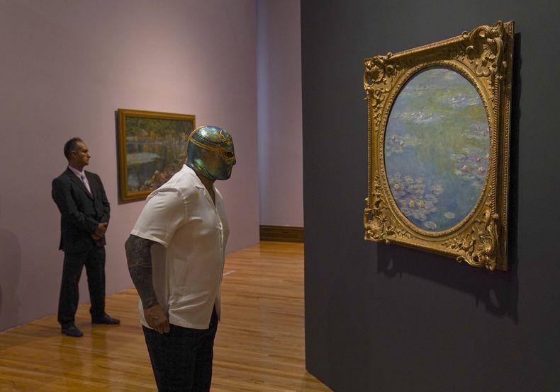 El luchador mexicano CintaDeOro observa una pintura de Claude Monet durante la inauguración de la exposición “Monet. Luces del Impresionismo” en la Ciudad de México el 26 de abril de 2023. (Foto AP/Fernando Llano)