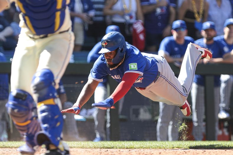 Vladimir Guerrero Jr., derecha, de los Azulejos de Toronto, se lanza al plato para anotar mientras el receptor de los Marineros de Seattle, Cal Raleigh, izquierda, espera por el tiro durante la 10ma entrada del juego de béisbol del domingo 7 de julio de 2024, en Seattle. (AP Foto/Jason Redmond)
