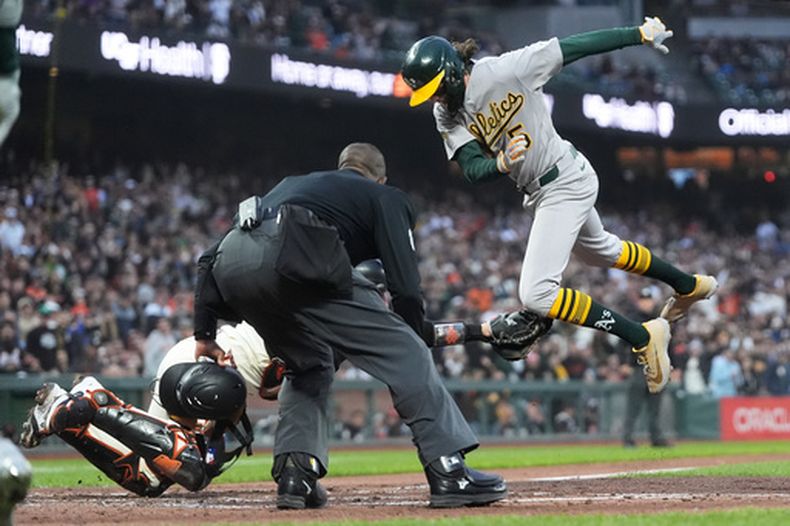 El umpire Ramón de Jesús, centro, observa al receptor de los Gigantes de San Francisco, izquierda, intentar poner out a Jacob Wilson, derecha, de los Atléticos en la quinta entrada del juego de béisbol de Grandes Ligas, el miércoles 24 de junio de 2026, en San Francisco. (AP Foto/Jeff Chiu)