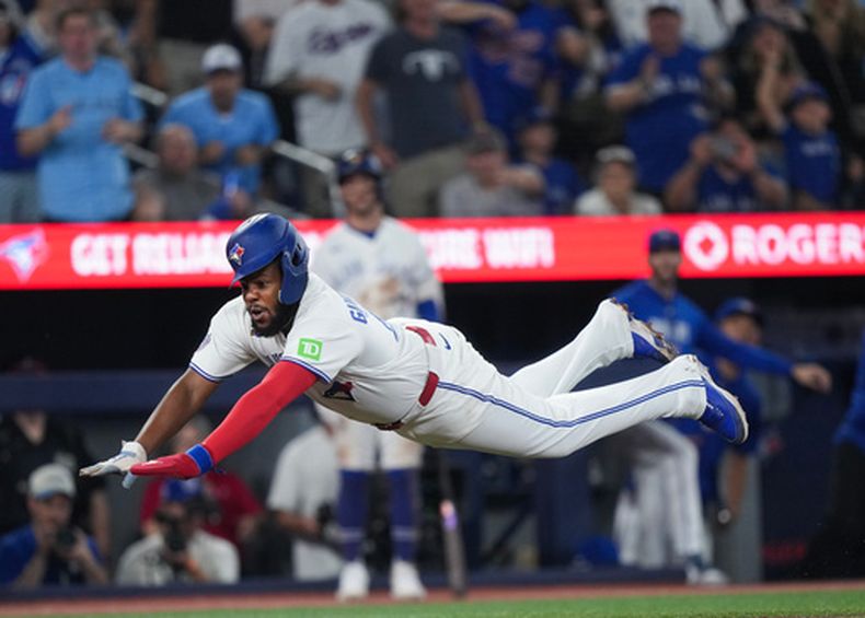 Vladimir Guerrero Jr. (27), de los Azulejos de Toronto vuela mientras se barre de frente para anotar una carrera superando al receptor Adley Rutschman (no en la imagen), de los Medias Rojas de Boston, durante la novena entrada del juego de béisbol de Grandes Ligas, el miércoles 12 de agosto de 2026, en Toronto. (Nathan Denette/The Canadian Press via AP)