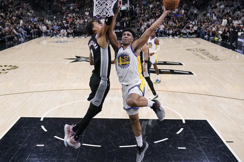 Trayce Jackson-Davis (32), de los Warriors de Golden State, ataca la canasta llevándose por delante a Victor Wembanyama (1), de los Spurs de San Antonio, durante la segunda mitad del juego de baloncesto de la NBA, en San Antonio, el lunes 11 de marzo de 2024. (AP Foto/Eric Gay)