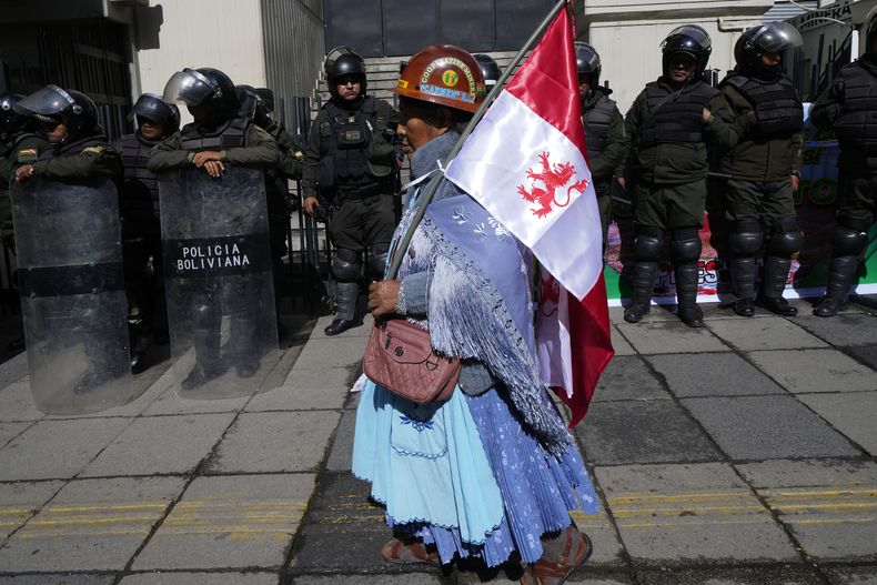 Una mujer minera camina por delante de policías que hacen guardia frente al Ministerio de Economía y Minería, en una protesta para reclamar al gobierno soluciones a la falta de combustibles y a la crisis económica, en La Paz, Bolivia, el miércoles 23 de abril de 2025. (AP Foto/Juan Karita)