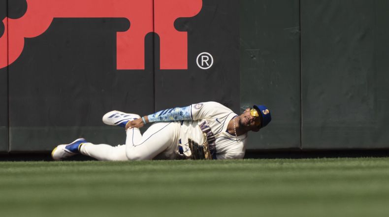 Julio Rodríguez, jardinero central de los Marineros de Seattle, se sujeta el tobillo derecho después de chocar contra la barda tratando de atrapar un elevado durante la sexta entrada del juego de béisbol en contra de los astros de Houston, el domingo 21 de julio de 2024, en Seattle. (AP Foto/Stephen Brashear)