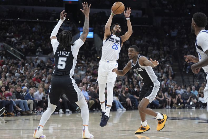 Spencer Dinwiddie (26), de los Mavericks de Dallas, pasa el balón sobre DeAaron Fox (4) y Stephon Castle (5), de los Spurs de San Antonio, durante la primera mitad del juego de baloncesto de la NBA, el lunes 10 de marzo de 2025, en San Antonio. (AP Foto/Eric Gay)