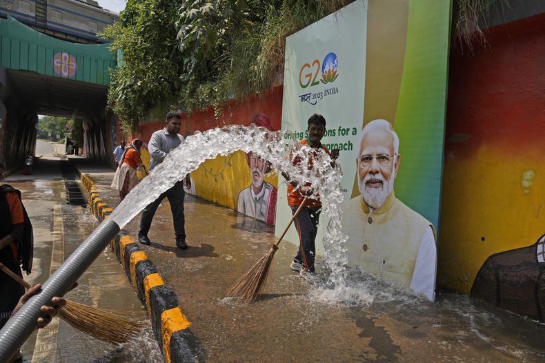 Trabajadores municipales lavan una acera junto a un cartel con la imagen del primer ministro indio Narendra Modi antes de la cumbre del Grupo de los Veinte a realizarse en su país esta semana, el jueves 7 de septiembre de 2023, en Nueva Delhi, India. (AP Foto/Manish Swarup)