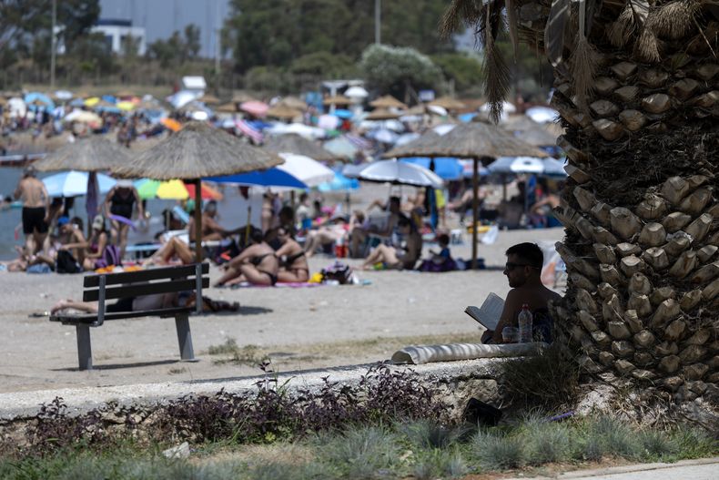 ARCHIVO - Un hombre lee un libro bajo la sombra de un árbol en una playa del suburbio de Glyfada, en Atenas, Grecia, el sábado 15 de julio de 2023. (AP Foto/Yorgos Karahalis, Archivo)