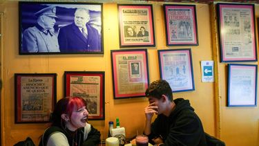 Una pareja está sentada en el Café Crónica, donde cuelga en la pared una foto del dictador Augusto Pinochet y del expresidente Patricio Aylwin, así como antiguas portadas de periódicos, en Santiago de Chile, el jueves 6 de noviembre de 2025. (AP Foto/Esteban Félix)