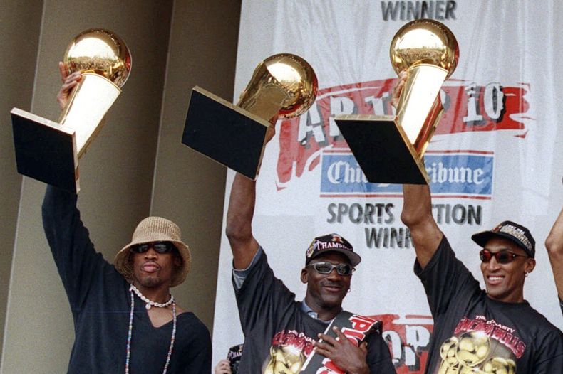 ARCHIVO - De izquierda a derecha, Dennis Rodman, Michael Jordan y Scottie Pippen, exjugadores de los Bulls de Chicago, sostienen tres de los trofeos del equipo, durante una ceremonia realizada el 16 de junio de 1997 (AP Foto/Michael Conroy, archivo)