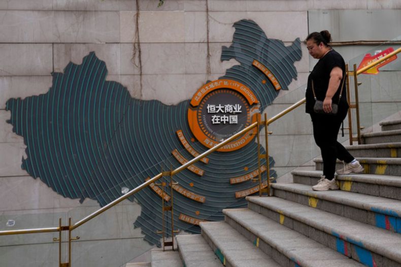 ARCHIVO - Una mujer camina junto a un mapa que muestra proyectos inmobiliarios de Evergrande en China, mientras se dirige a la plaza urbana Evergrande en Beijing el 18 de septiembre de 2023. (AP Foto/Andy Wong, Archivo)