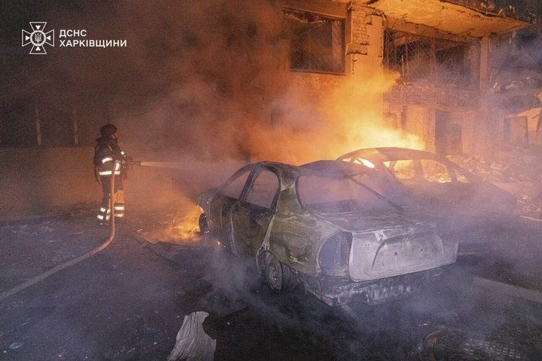 En esta imagen proporcionada por los Servicios Ucranianos de Emergencia el jueves 12 de junio de 2025, un rescatista apaga un incendio en un auto cerca de un edificio dañado por un ataque ruso en Járkiv, Ucrania. (Servicios Ucranianos de Emergencia via AP)